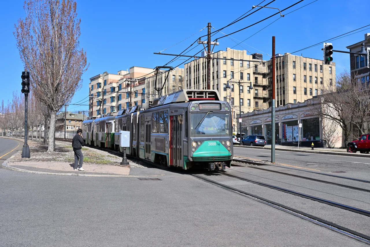 Green Line train beside apartment buildings and storefronts near Sutherland Road in Brighton, Boston