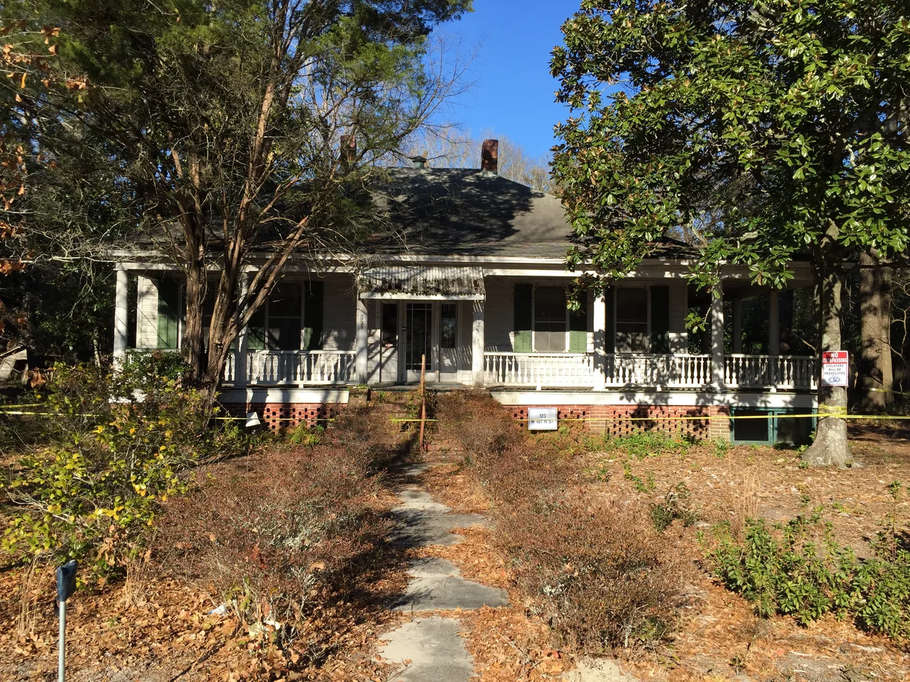 Long front porch and low roof of a house shaded by trees on West 1st North Street in Summerville