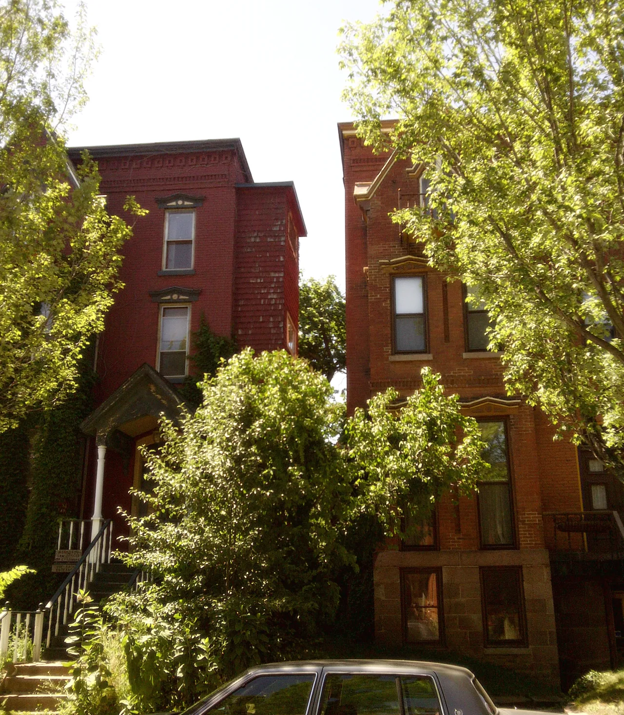 Two narrow brick houses with front steps and mature trees in Rochester’s Corn Hill neighborhood