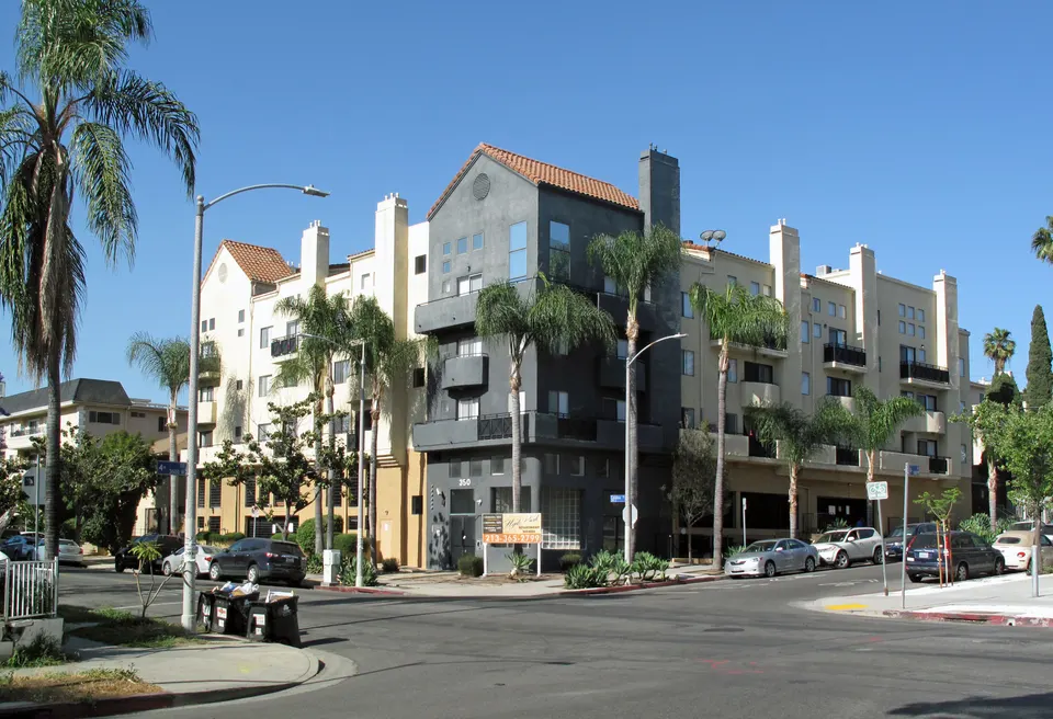 A five-story apartment building with balconies and palm trees at a street corner in Koreatown, Los Angeles
