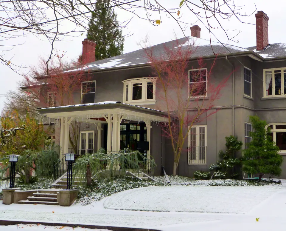 A two-story stucco fourplex apartment building with a covered entry, bay windows and four chimneys, on a snowy lawn
